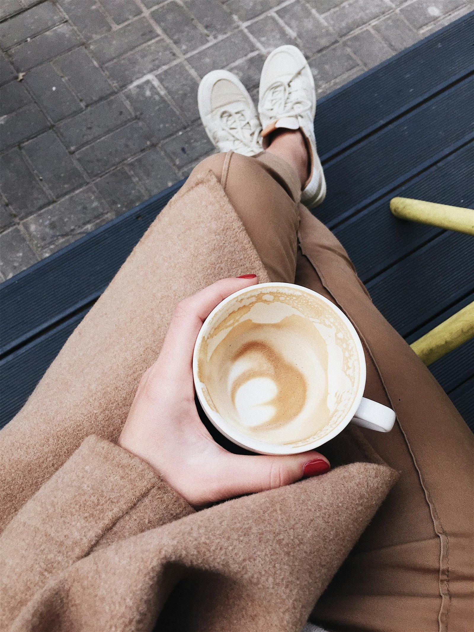 Overhead view of a person holding a latte while sitting on an outdoor bench, capturing a relaxed moment.